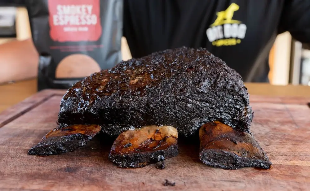 Charcoal grilled rack of lamb on a cutting board with Brad in the background.